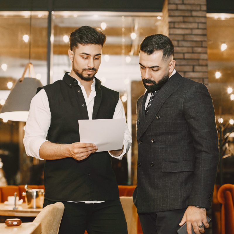 Handsome man in a black suit. Businessmen working in a cafe. People stands and looks in a documents.